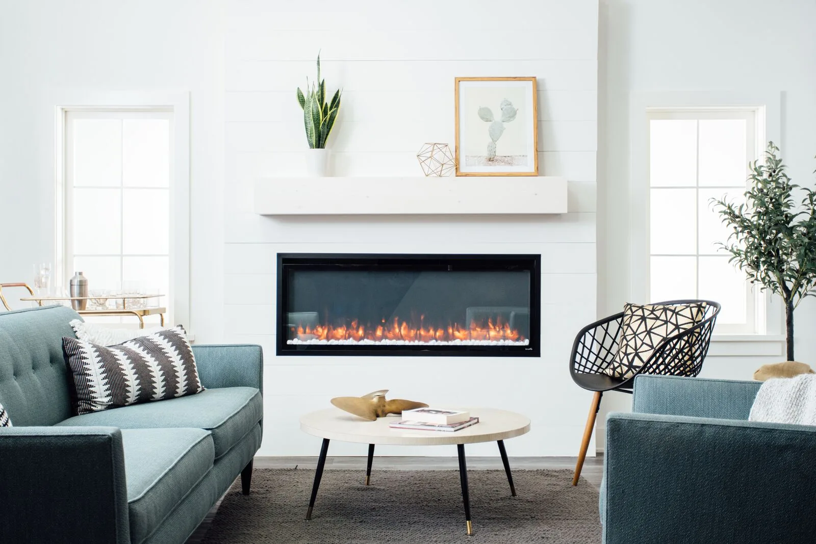 A SimpliFire Allusion linear electric fireplace in a white shiplap wall over a teal sofa (manufacturer lifestyle photo)