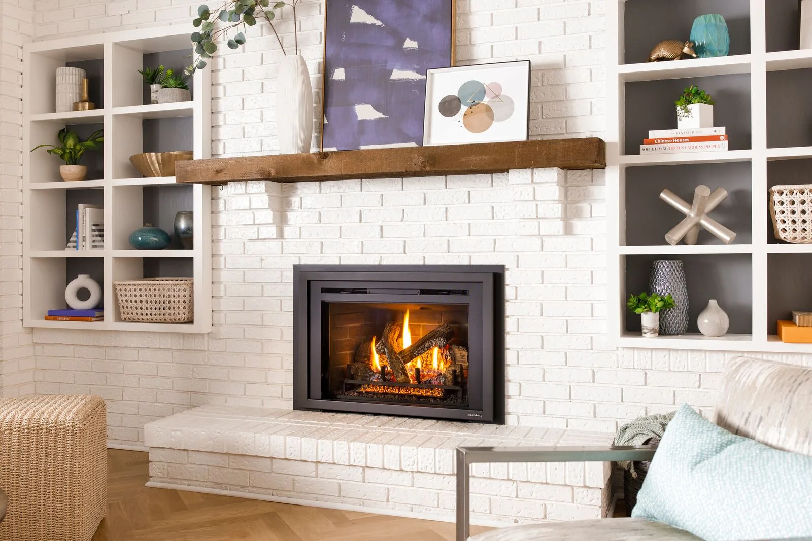 A Heat & Glo gas insert burning in a painted white brick fireplace with built-in shelves (manufacturer lifestyle photo)
