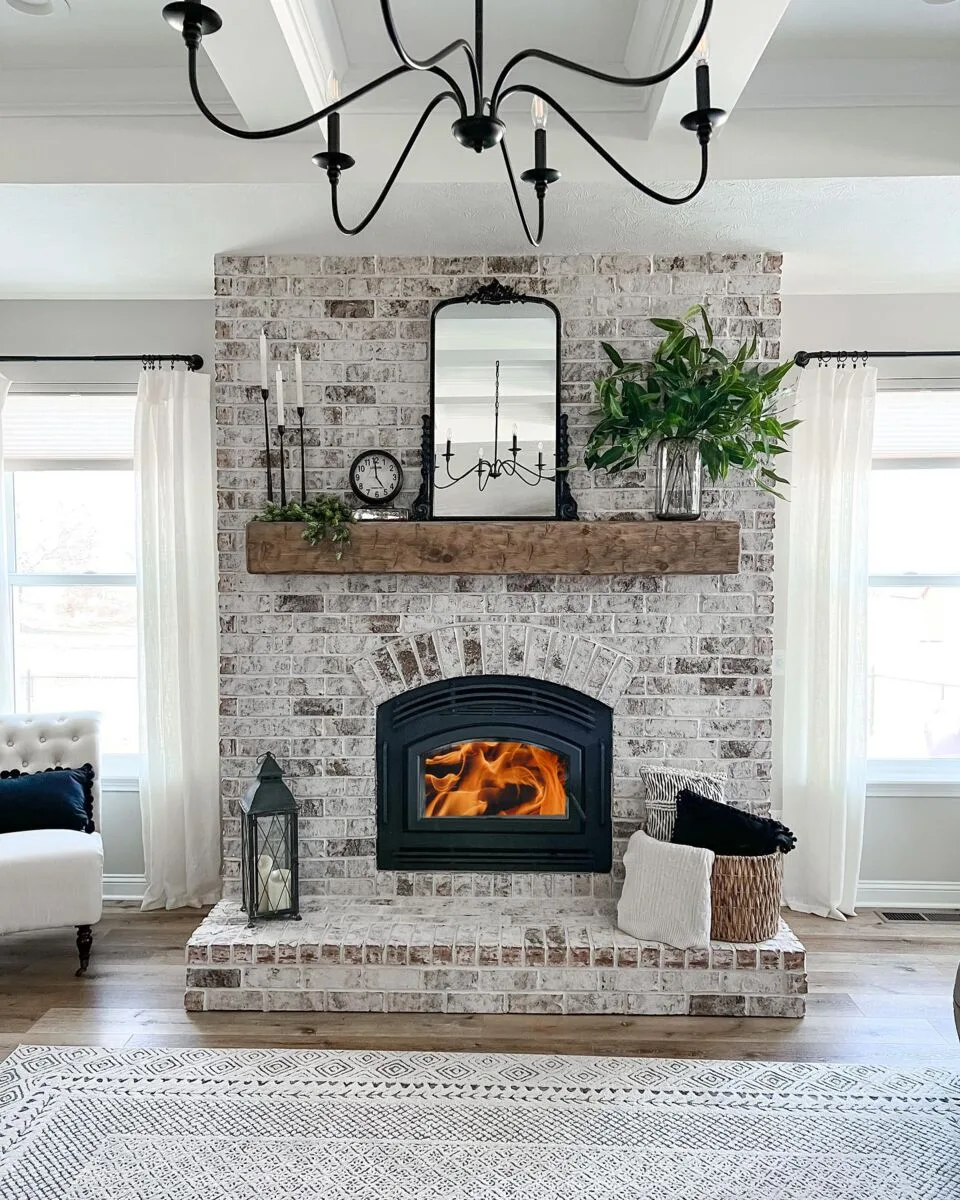 A Quadra-Fire Pioneer II wood fireplace burning in a whitewashed brick wall under a timber mantel (manufacturer lifestyle photo)