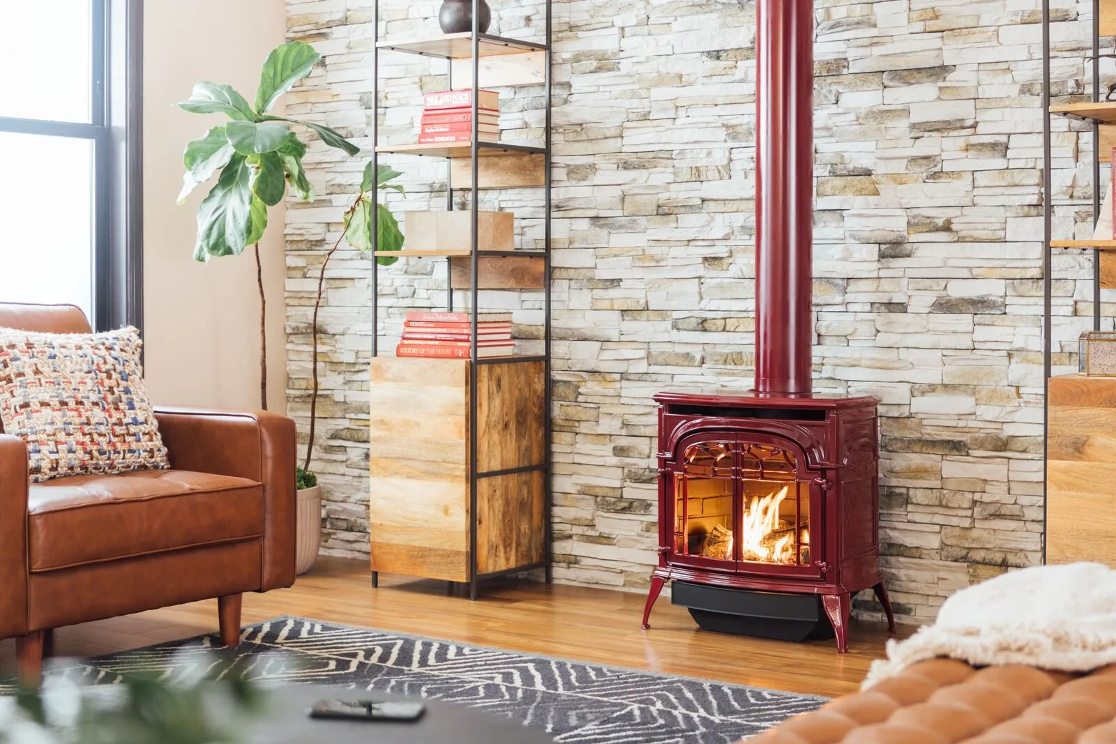 A red Vermont Castings Stardance gas stove on a hearth pad against a stacked-stone wall (manufacturer lifestyle photo)