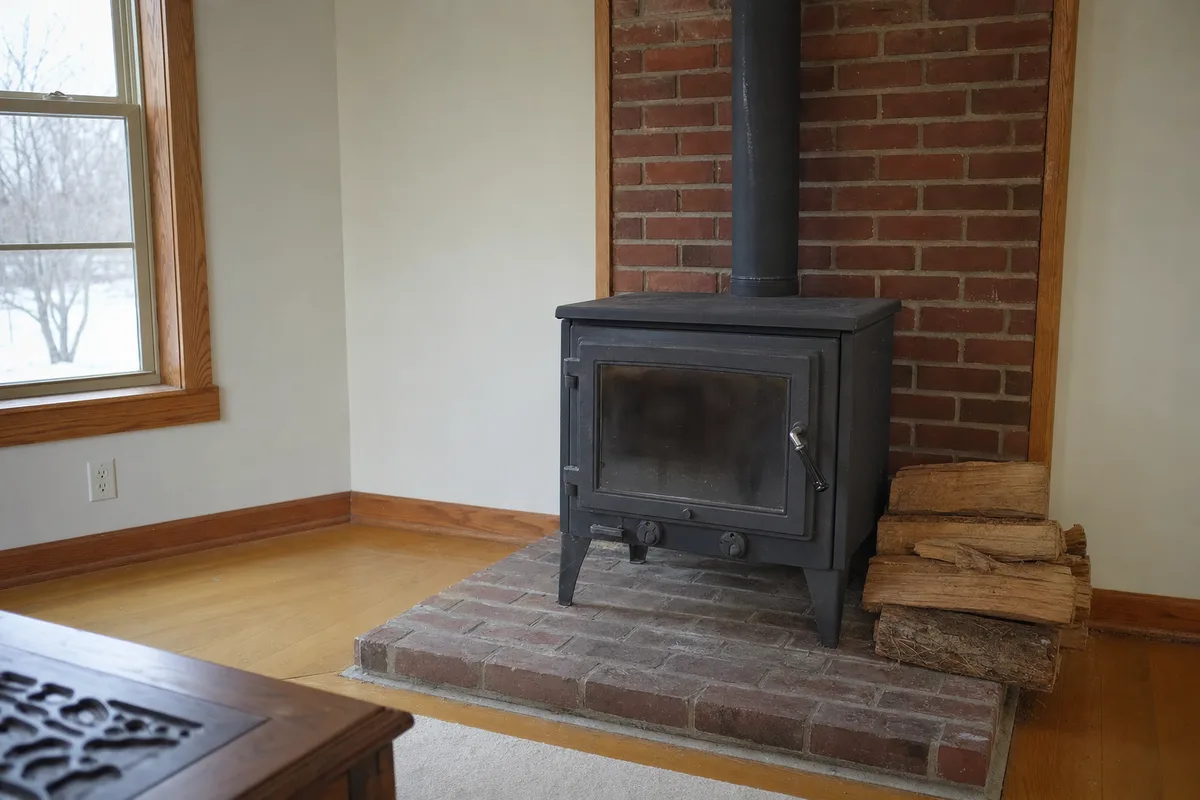 An old black wood stove on a brick hearth beside a window